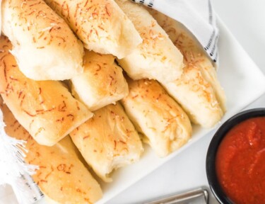 Top view of breadsticks on a plate next to a cup of pizza sauce