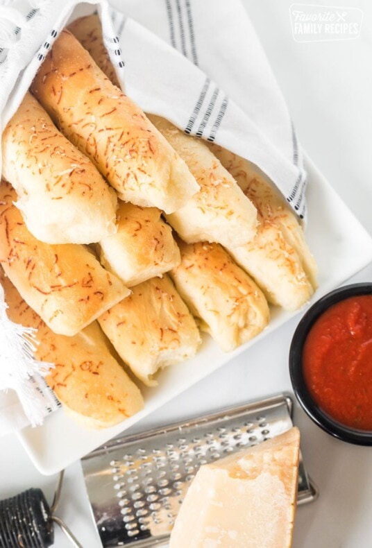 Top view of breadsticks on a plate next to a cup of pizza sauce