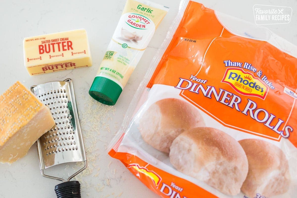 A bag of frozen rolls, garlic paste, a stick of butter, and parmesan cheese on a table top.