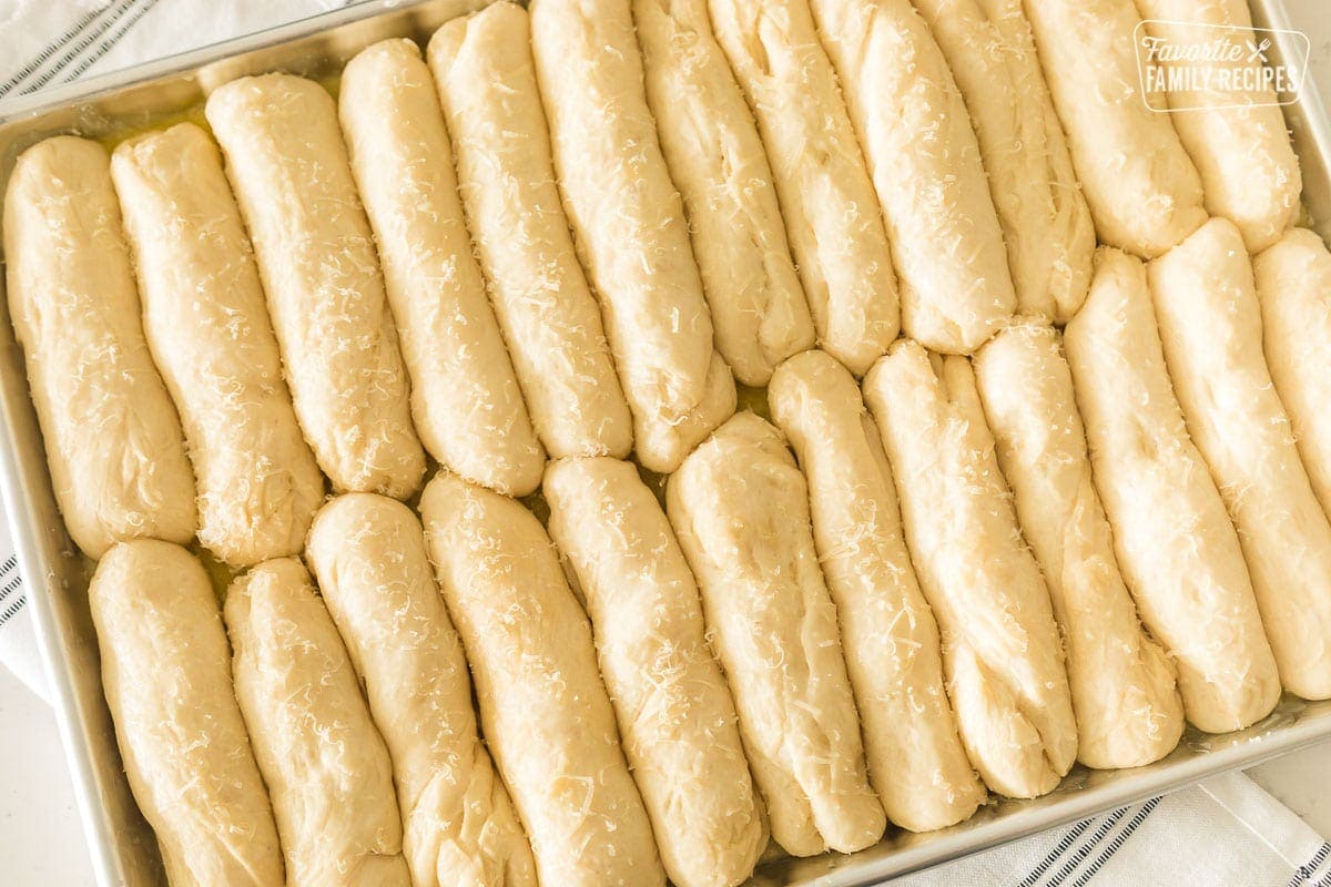 Uncooked, thawed breadsticks in a pan that have risen and are ready for baking