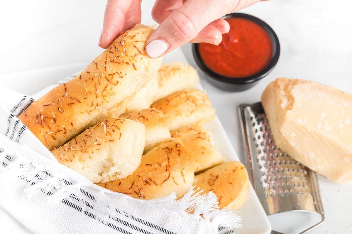A hand taking a light and fluffy breadstick from a bundle of breadsticks on a plate