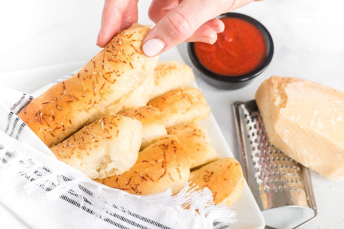 A hand taking a light and fluffy breadstick from a bundle of breadsticks on a plate.