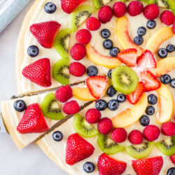 Serving spatula taking out a slice of easy fruit pizza from the whole.