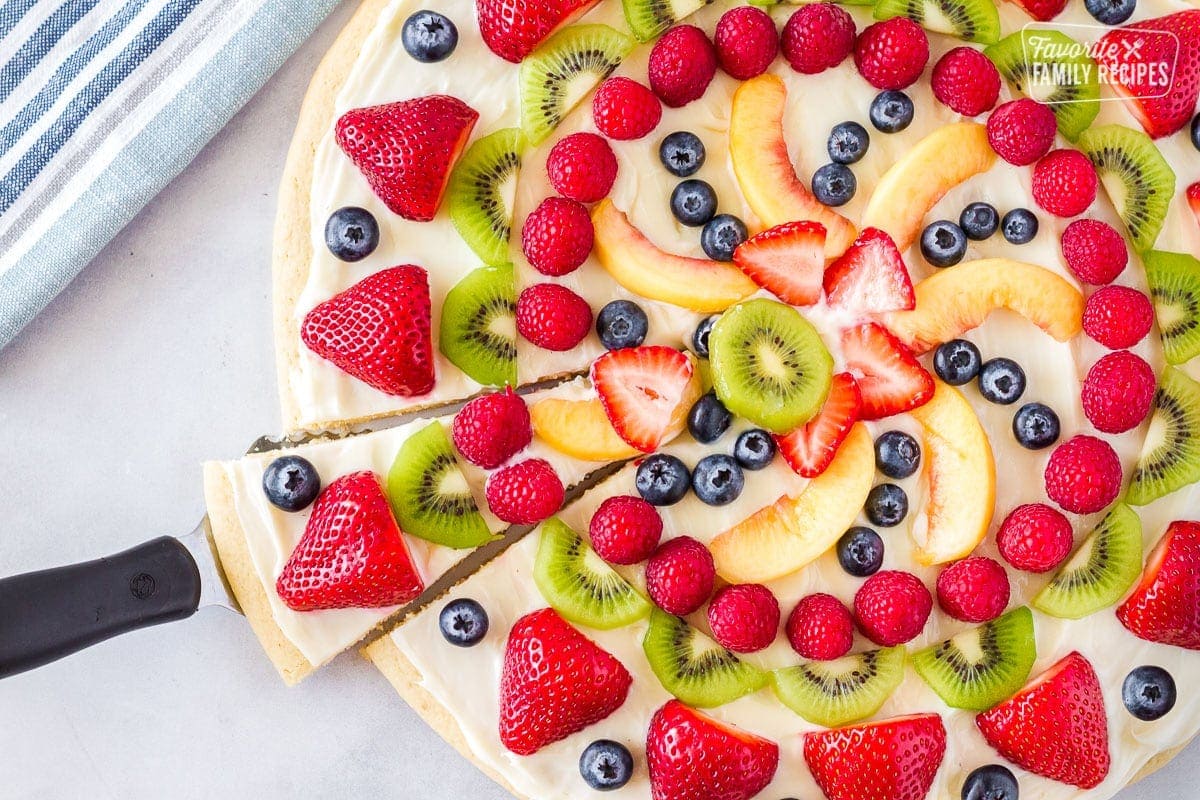 Serving spatula taking out a slice of easy fruit pizza from the whole.