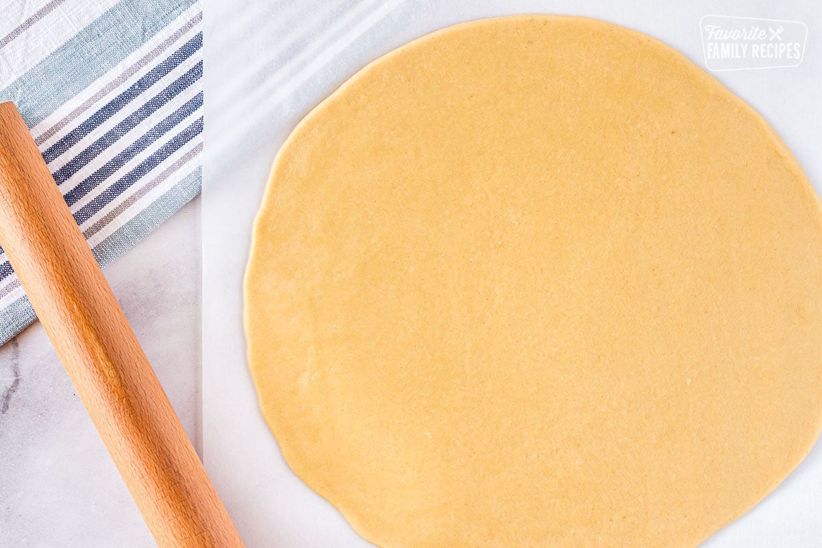 Large circular flattened cookie dough with a rolling pin on the side to make easy fruit pizza.