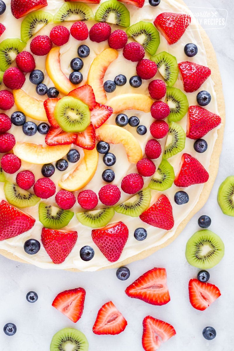 Easy dessert pizza topped with cream cheese icing and fresh fruit with extra fruit on the side.