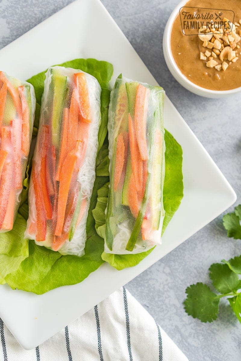 Three wrapped fresh spring rolls on a plate next to a bowl of peanut sauce
