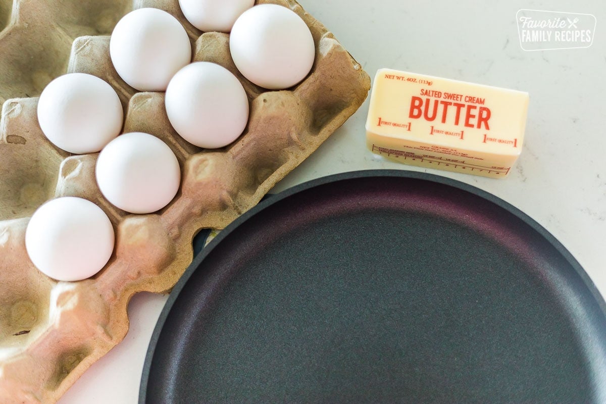 A carton of eggs, a stick of butter, and a frying pan on a counter top