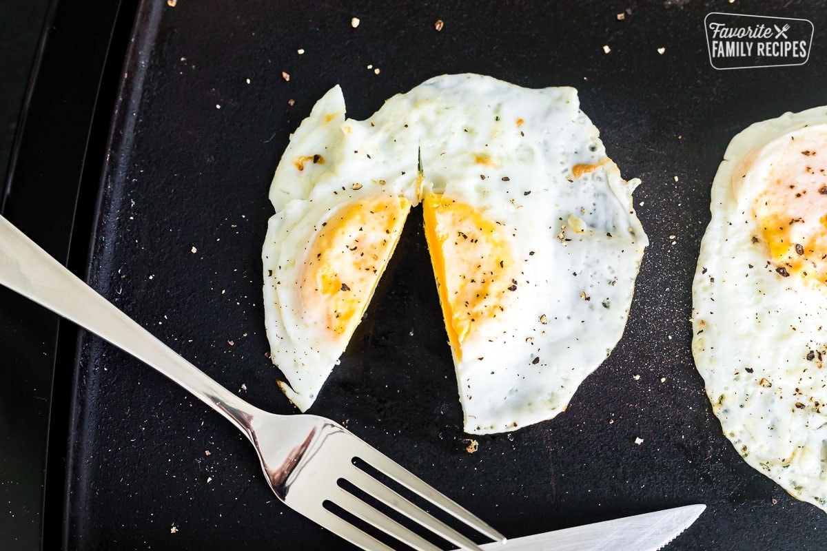 A fried egg on a griddle cooked to over hard. The egg is cut open to show hard center