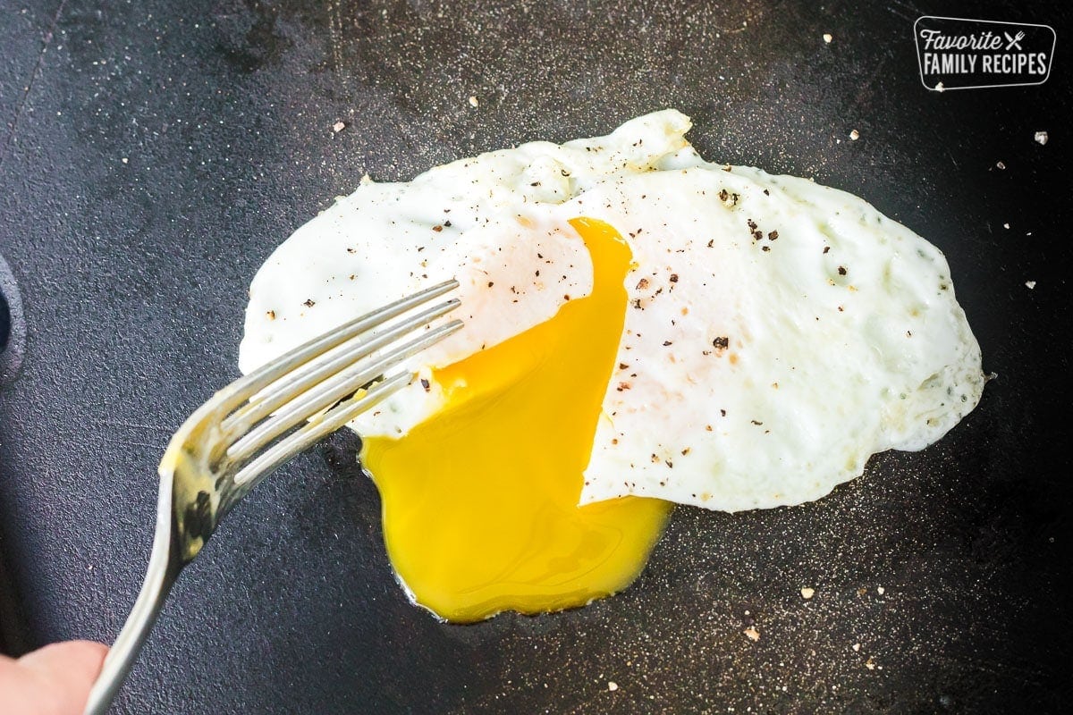 An over easy fried egg being pierced with a fork to show runny yolk