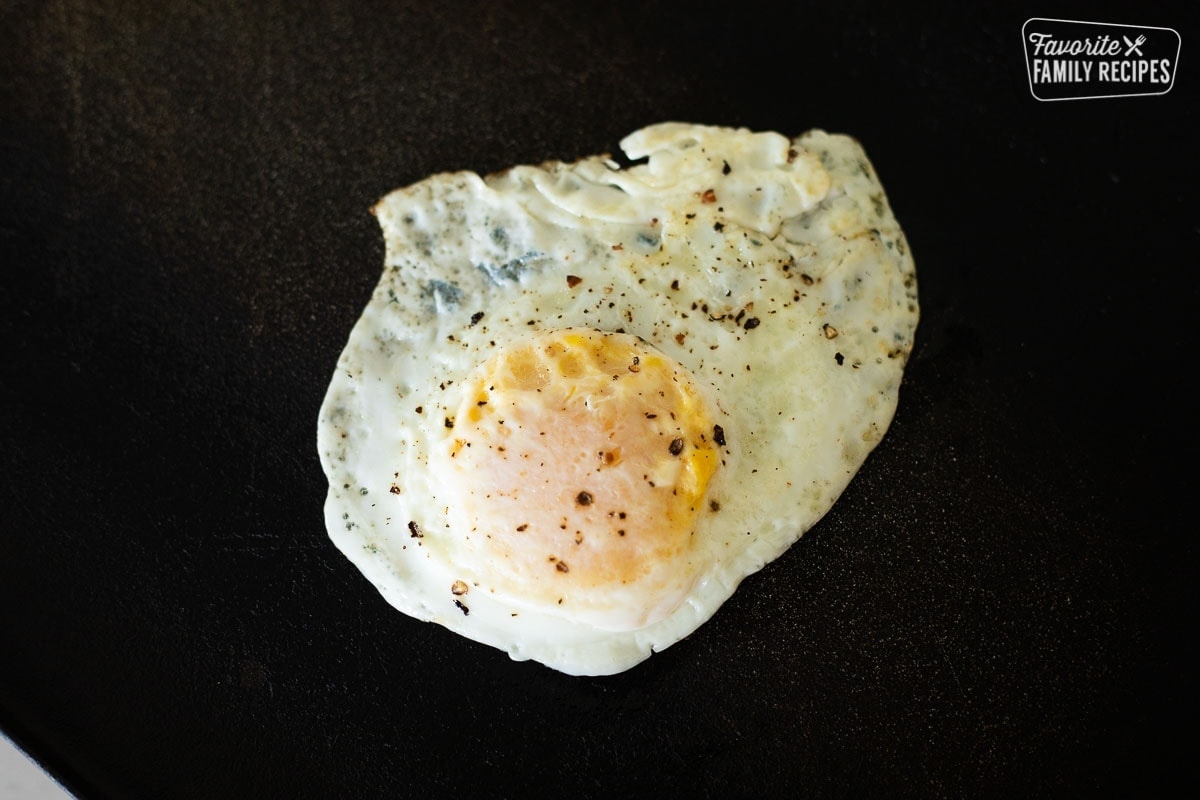 An egg cooked to over medium on a black frying pan