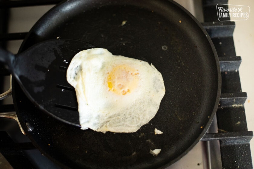 An egg being fried in a frying pan and being flipped with a black spatula