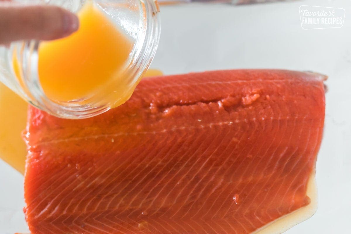 Orange juice being poured over a large cut of salmon