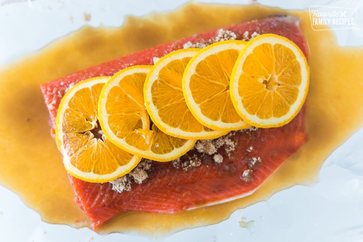 A large cut of salmon topped with orange juice, brown sugar, and orange slices