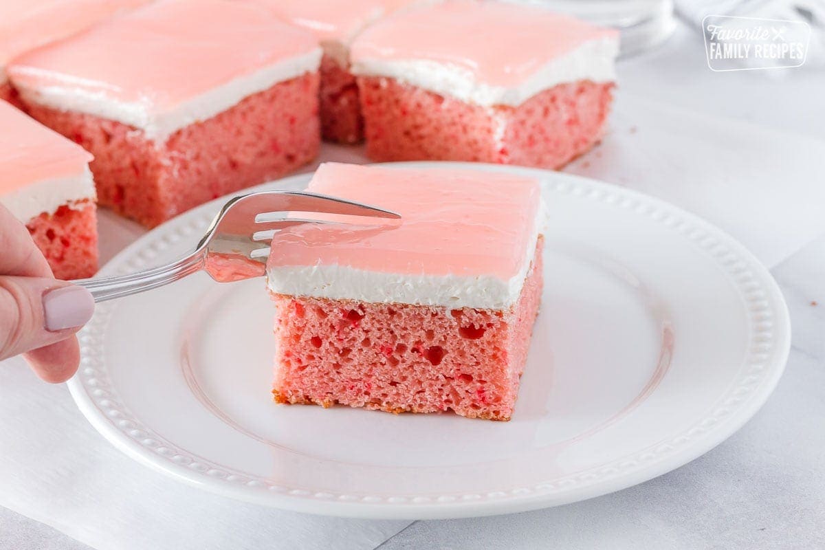 Fork slicing into a piece of pink Hawaiian guava cake with multiple slices behind.