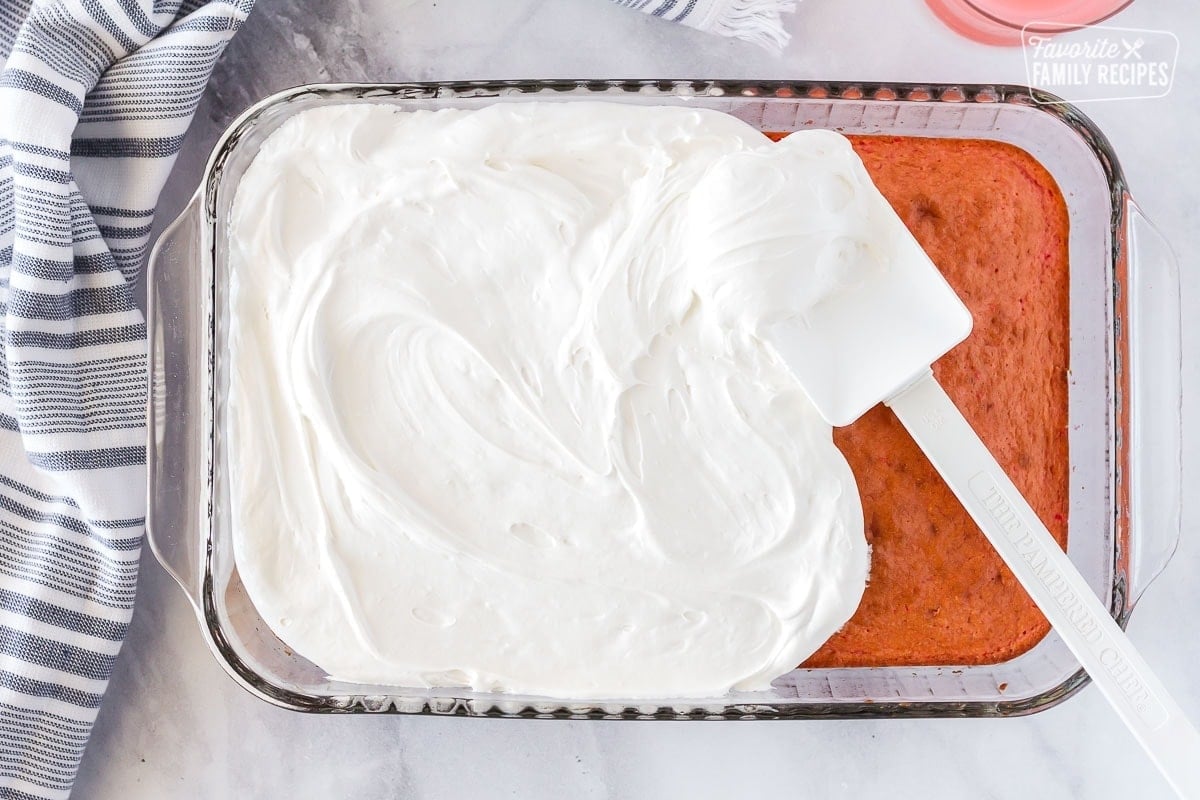 Spatula spreading whipped filling on prepared cake to make Hawaiian guava cake.