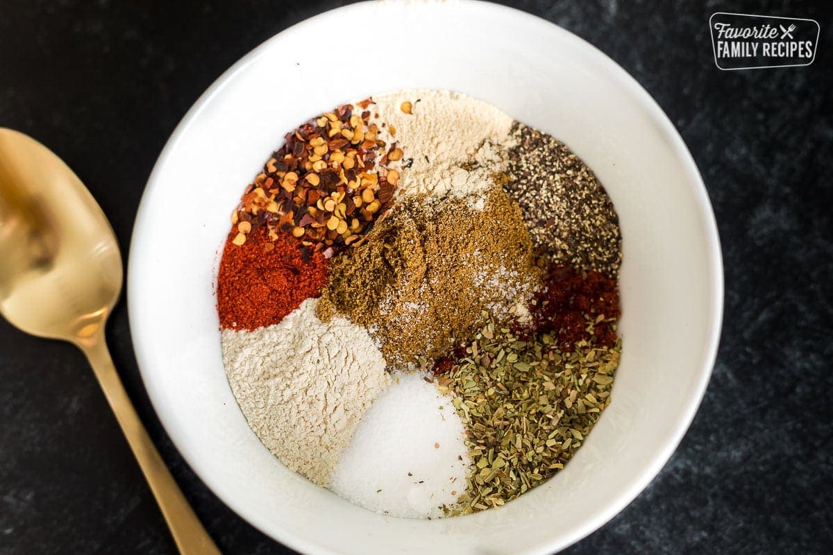 Ingredients to make homemade taco seasoning in a white bowl including chili powder, cumin, oregano, salt, and pepper