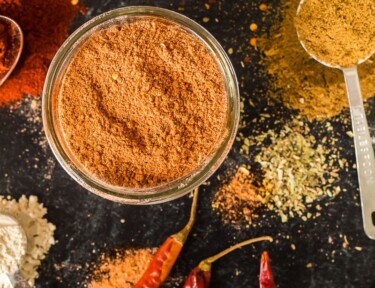 Taco seasoning in a jar with chilies and other ingredients on the table around it