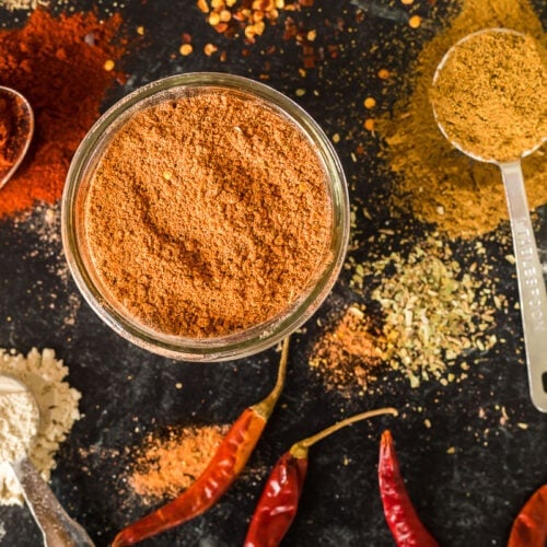 Taco seasoning in a jar with chilies and other ingredients on the table around it