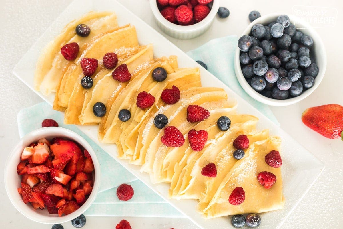 A top view of homemade crepes on a serving platter topped with raspberries and blueberries.