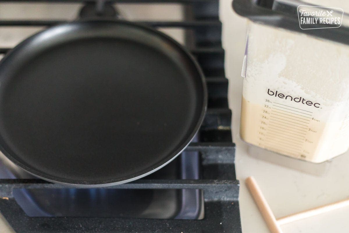 A crepe cooking pan next to a blender of crepe batter.