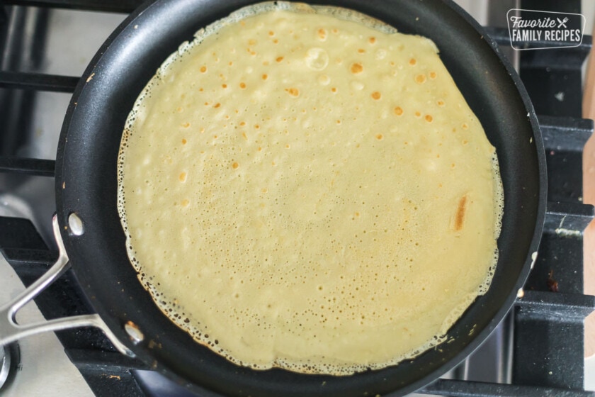 A crepe cooking in a black, flat cooking pan