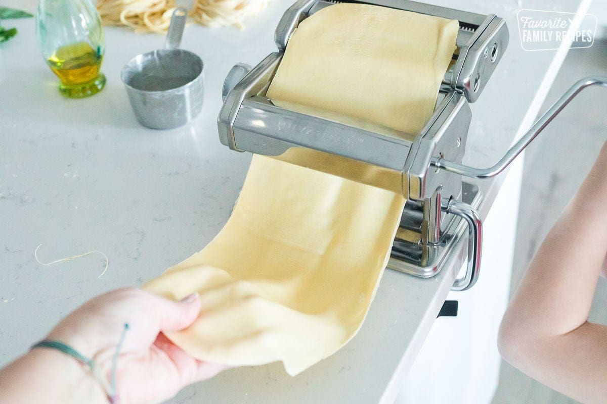 A sheet of pasta dough being fed through a pasta roller