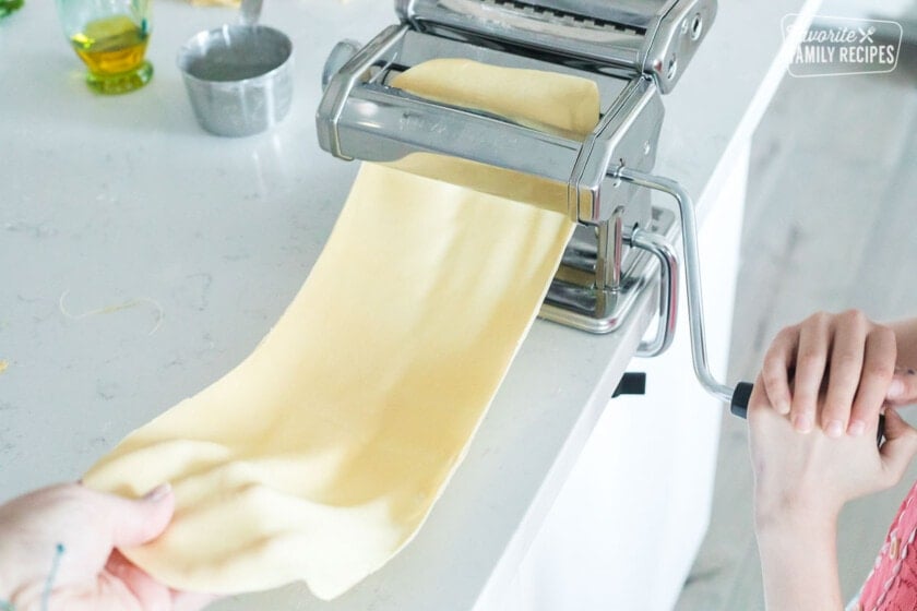 Sheets of pasta dough being fed through a pasta maker