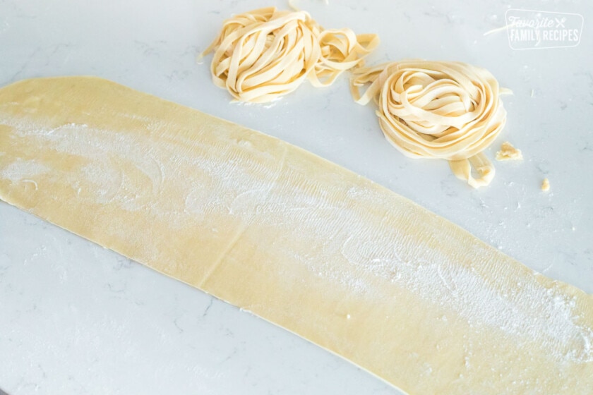 A flat sheet of pasta dough next to two nests of pasta noodles