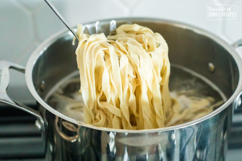 Homemade pasta noodles being lifted from a pot of boiling water