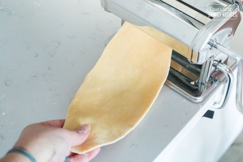 Pasta dough being fed through a pasta roller