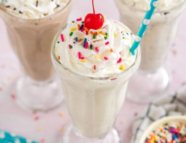 A vanilla milkshake with whipped cream, sprinkles and a cherry
