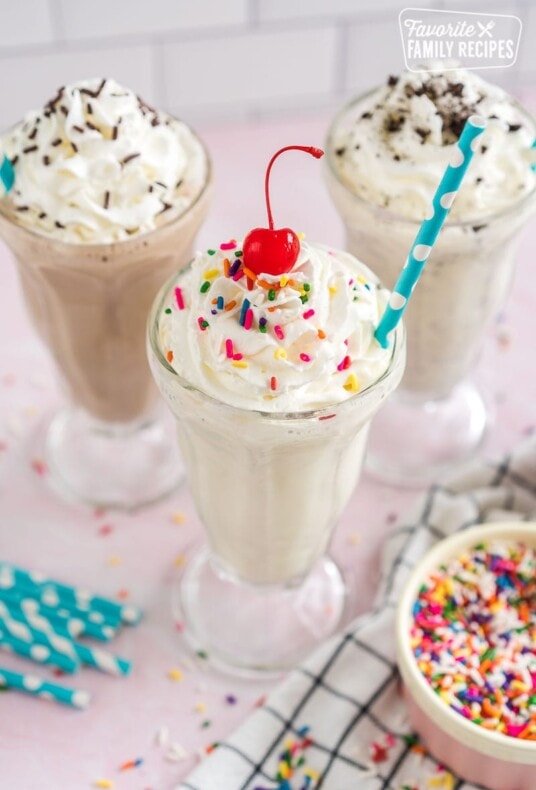 A vanilla milkshake with whipped cream, sprinkles and a cherry