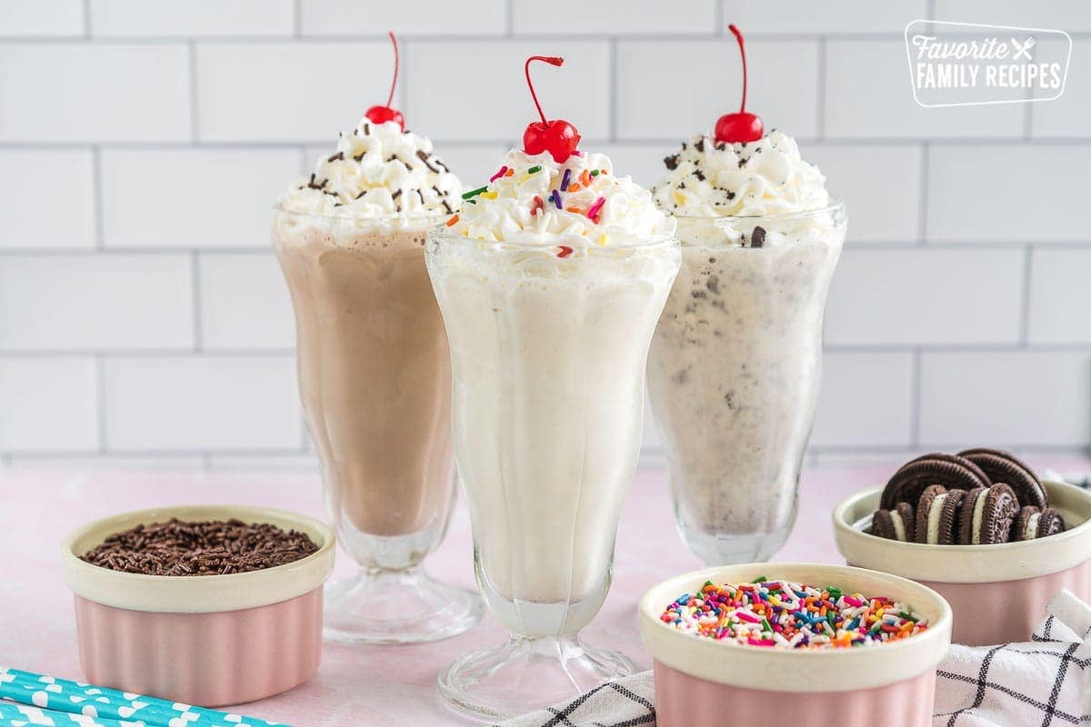 Three milkshakes topped with whipped cream, sprinkles, and cherries