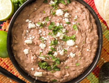 Homemade refried beans in a bowl next to some limes and queso fresco