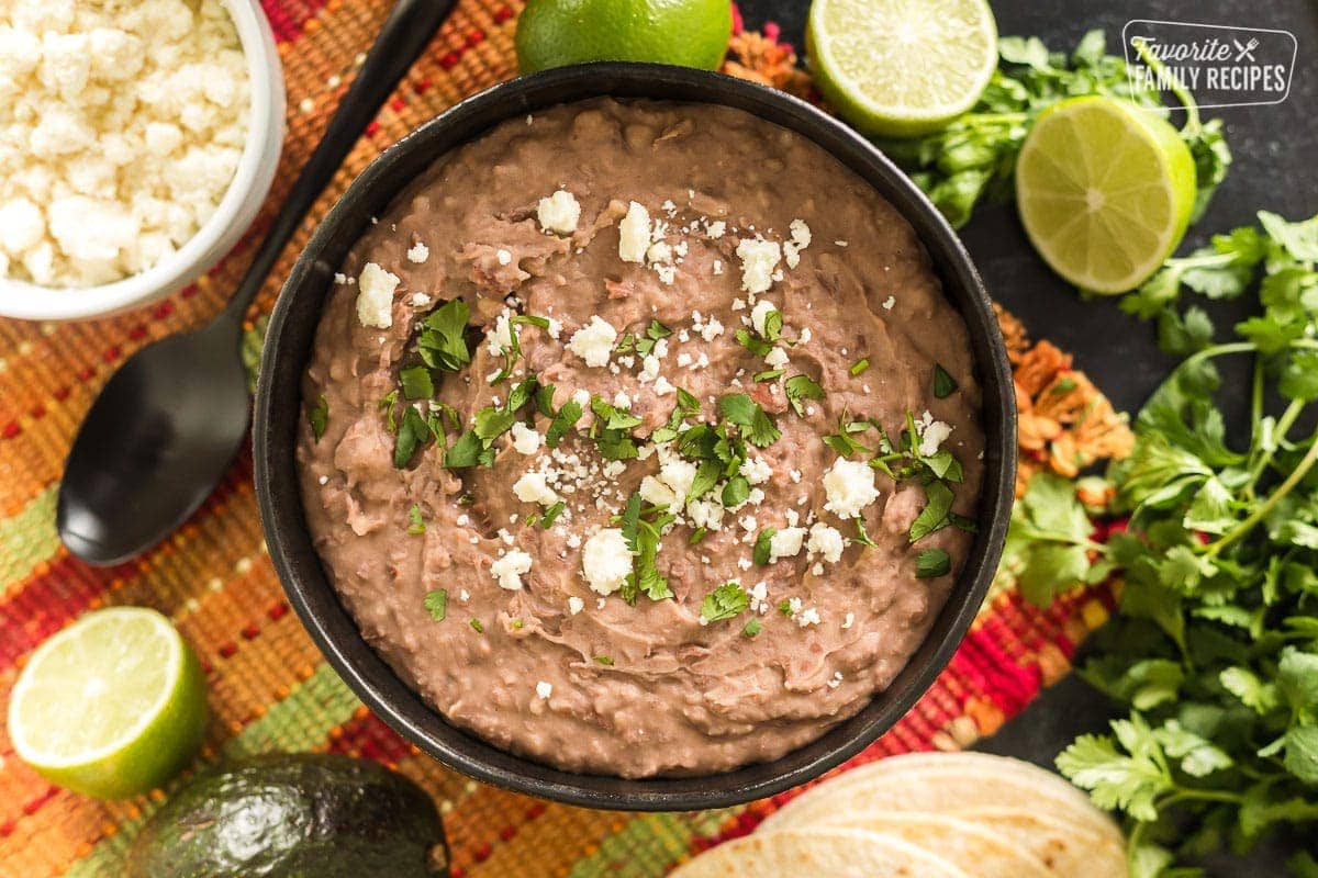 A bowl of homemade refried beans next to some limes and cilantro