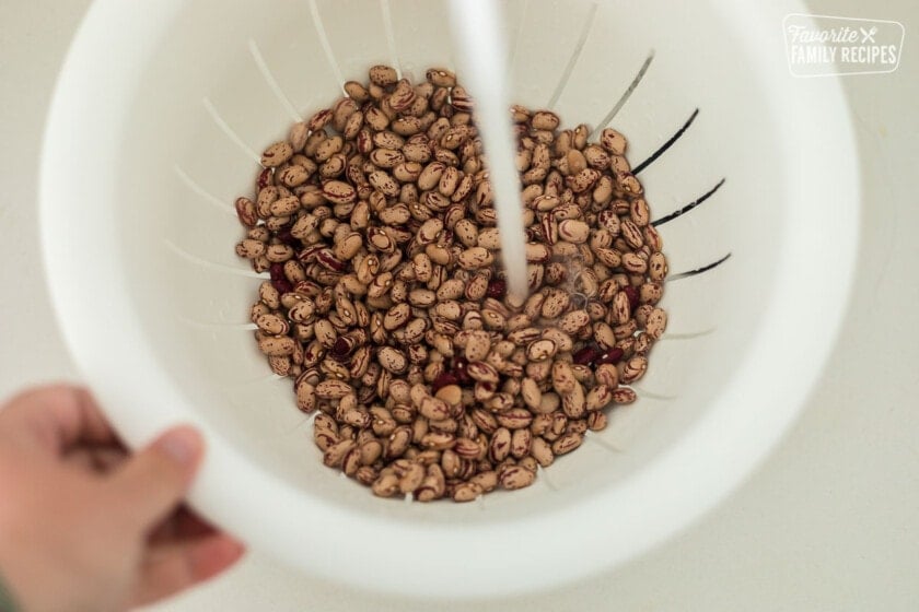 Dry pinto beans being rinsed in a colander in the sink