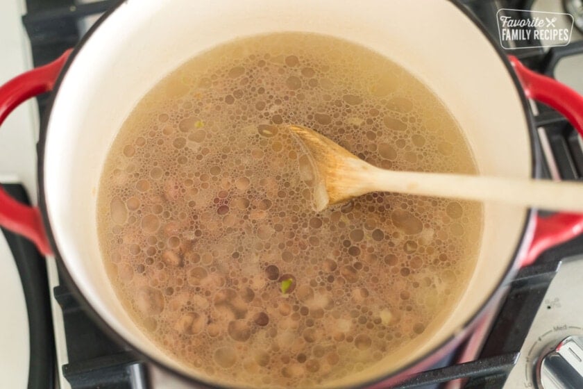 Dry pinto beans simmering in broth in a Dutch oven on the stove