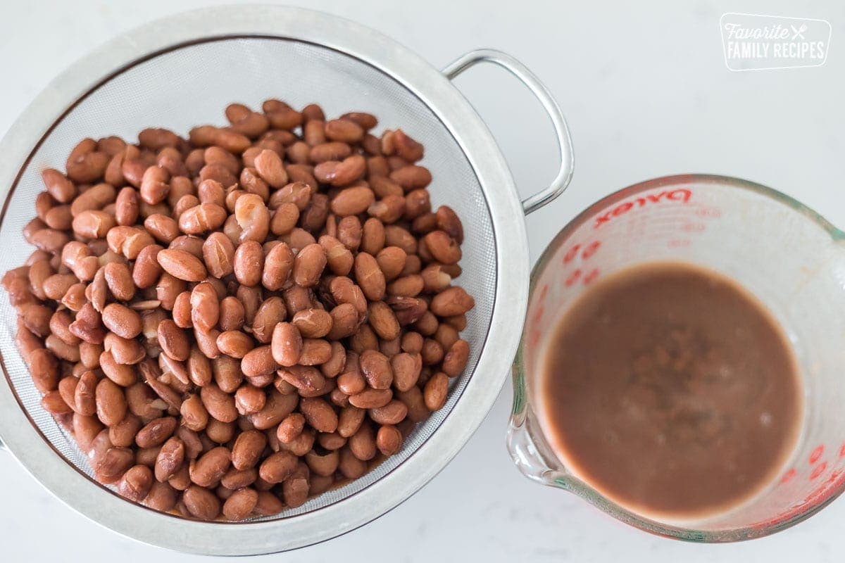 Pinto beans in a strainer next to a bowl of bean liquor