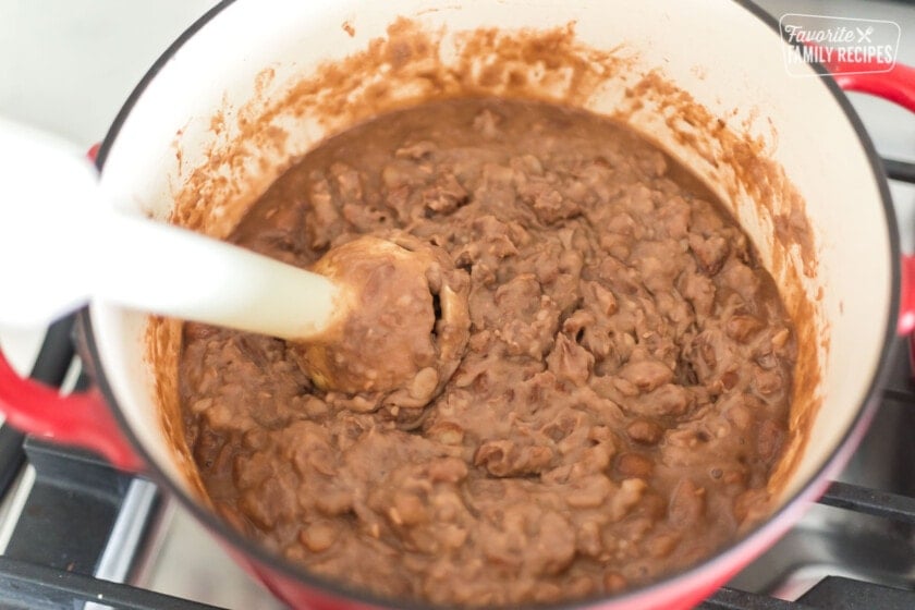 An immersion blender blending pinto beans into refried beans