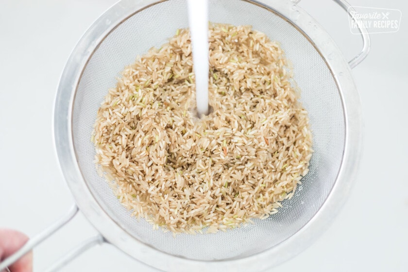 Brown rice being rinsed with water in a fine mesh strainer