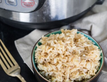 Brown rice in a small bowl next to an Instant Pot (Pressure Cooker)