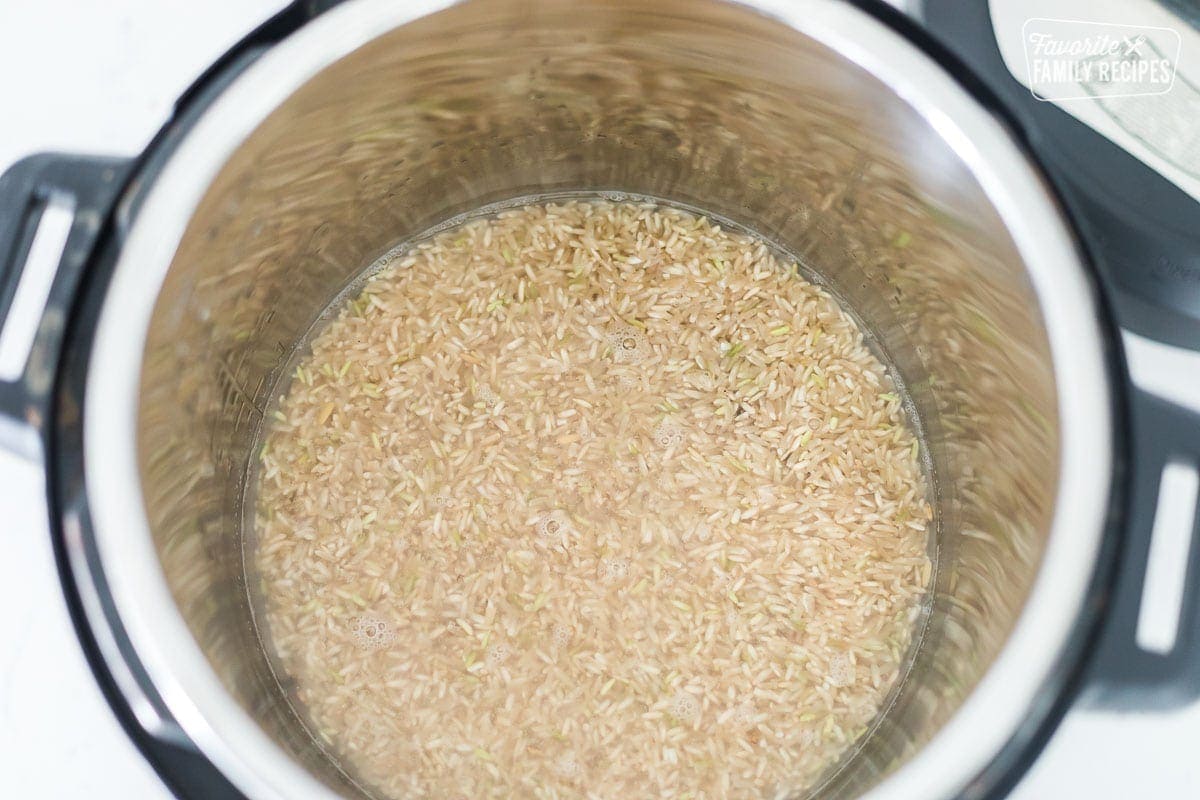 An instant pot with uncooked brown rice covered with water