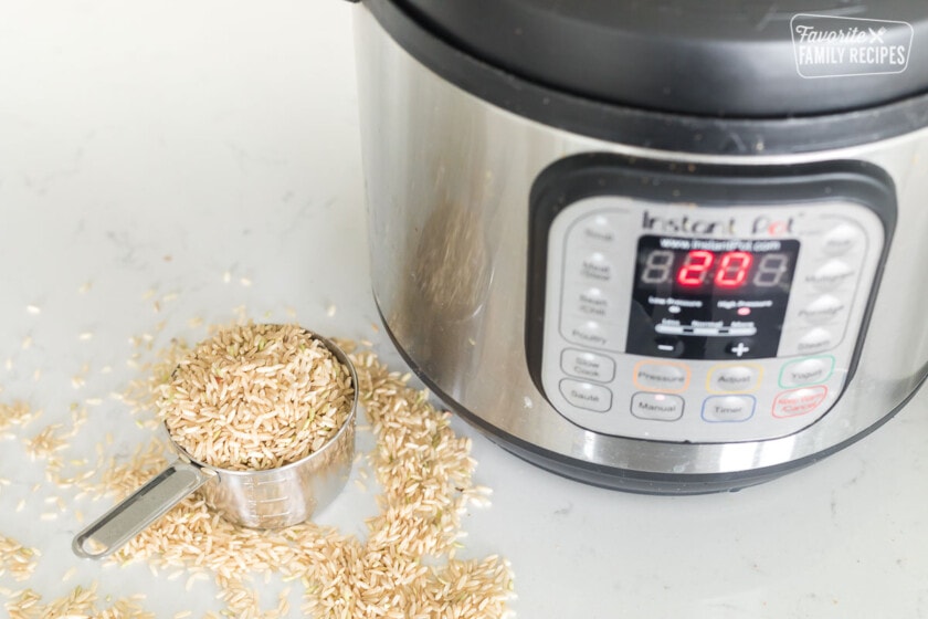 A measuring cup of uncooked brown rice next to an Instant Pot