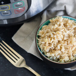 Cooked brown rice in a small bowl next to an Instant Pot