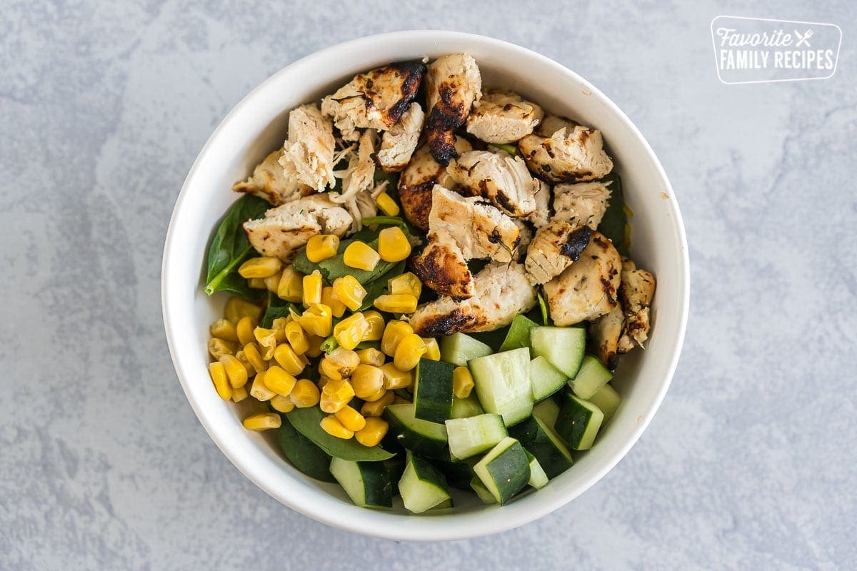 A large bowl with saffron rice, spinach, chicken, corn, and cucumbers