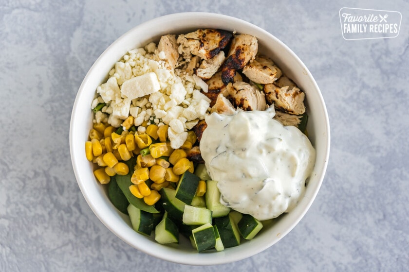A large bowl filled with saffron rice, spinach, chicken, corn, cucumbers, feta cheese, and tzatziki sauce