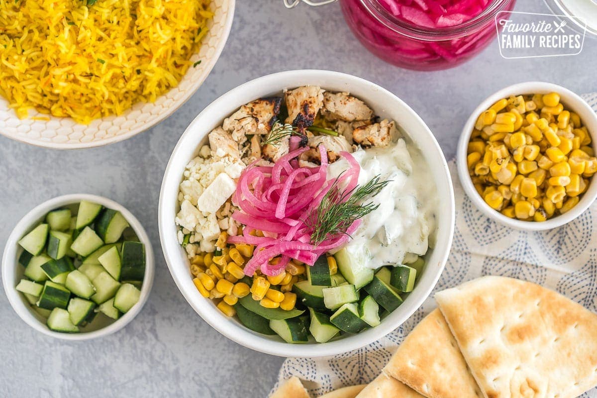 A Mediterranean bowl with saffron rice, spinach, chicken, corn, cucumbers, feta cheese, tzatziki sauce, pickled red onions, and fresh dill