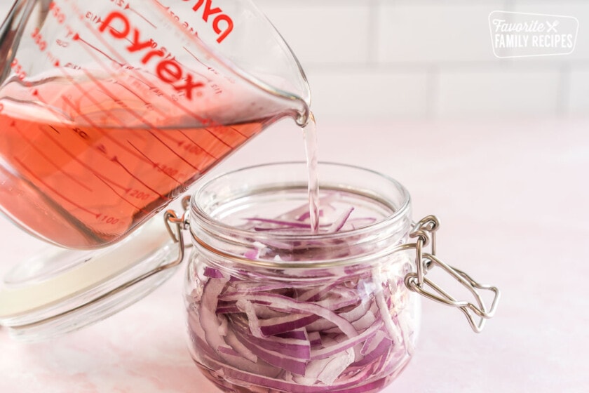 Pickling mixture being poured into a glass jar full of sliced red onions