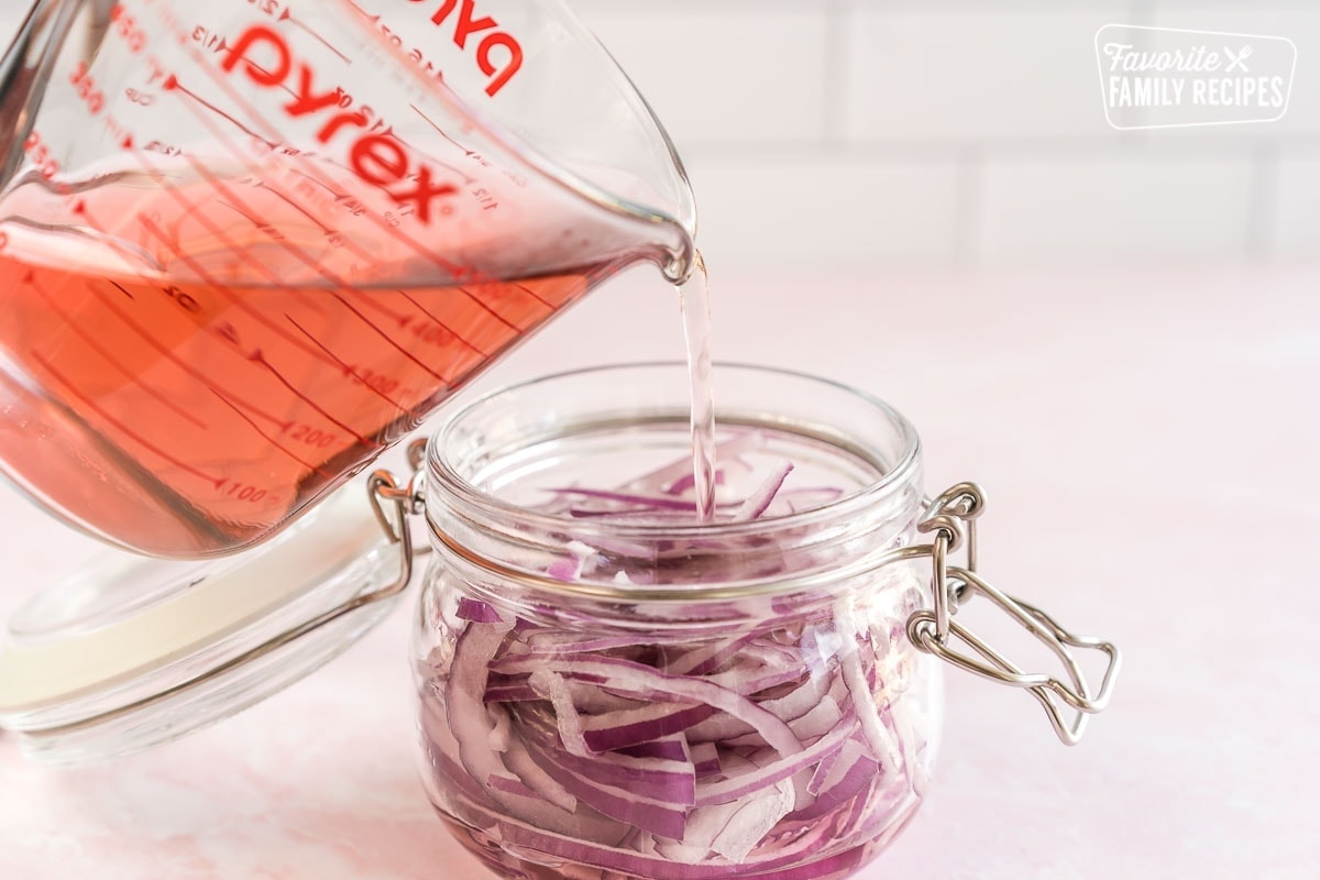 Pickling mixture being poured into a glass jar full of sliced red onions.